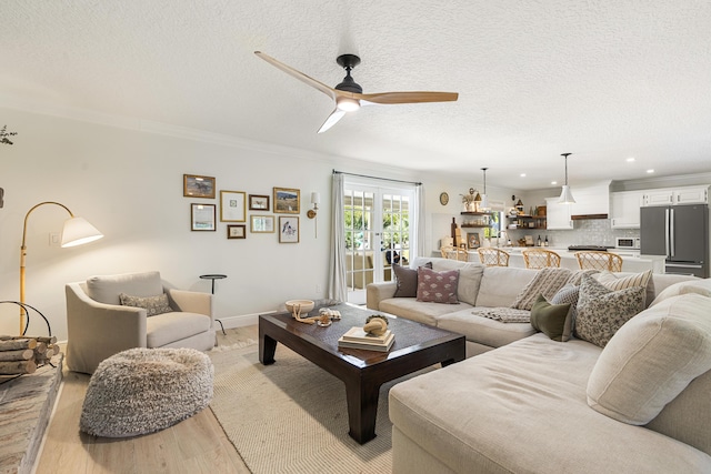 living room with a textured ceiling, french doors, light hardwood / wood-style floors, ornamental molding, and ceiling fan