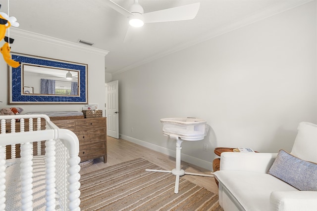 bedroom with ceiling fan, a nursery area, ornamental molding, and wood-type flooring