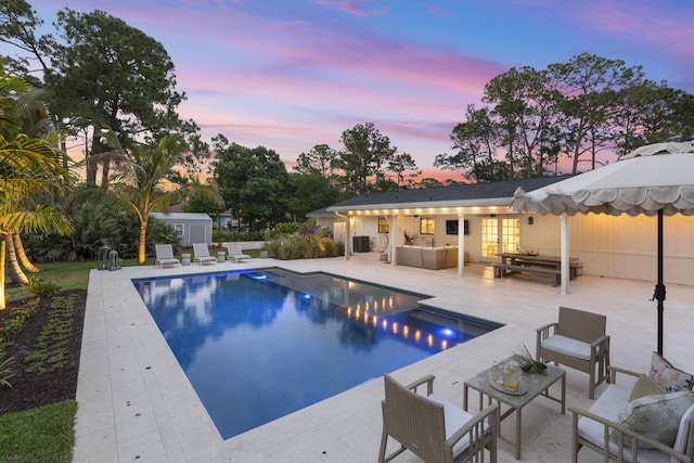 pool at dusk with an outdoor living space, an outbuilding, and a patio