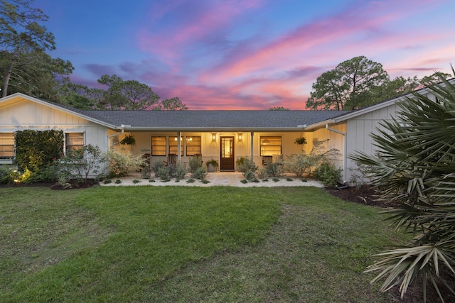 back house at dusk featuring covered porch and a yard