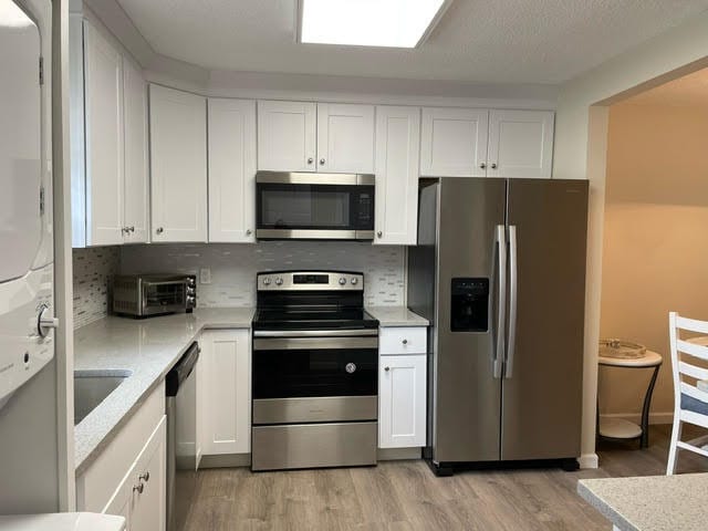 kitchen featuring white cabinets, light hardwood / wood-style flooring, backsplash, and stainless steel appliances