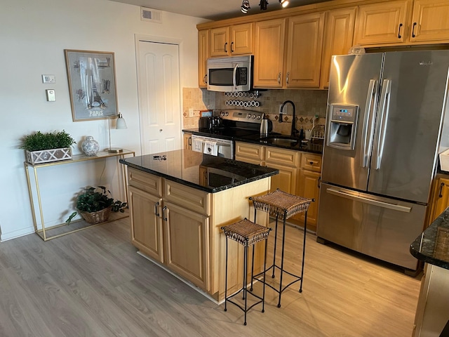 kitchen with dark stone counters, a kitchen island, light hardwood / wood-style flooring, sink, and appliances with stainless steel finishes