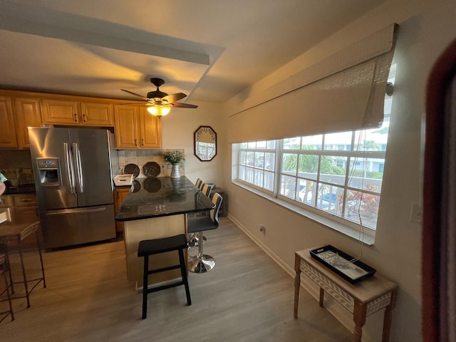 kitchen featuring light wood-type flooring, a kitchen bar, stainless steel fridge with ice dispenser, and decorative backsplash