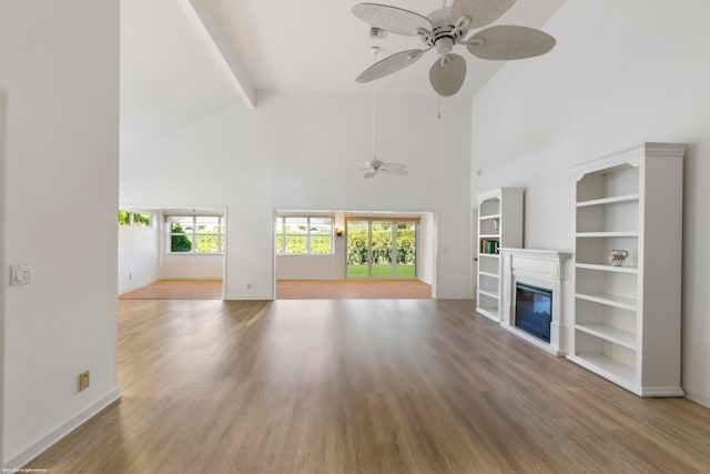 unfurnished living room with hardwood / wood-style floors, beamed ceiling, ceiling fan, and a towering ceiling