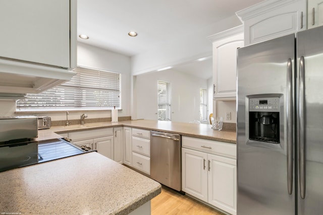 kitchen featuring light wood-type flooring, white cabinetry, kitchen peninsula, appliances with stainless steel finishes, and sink