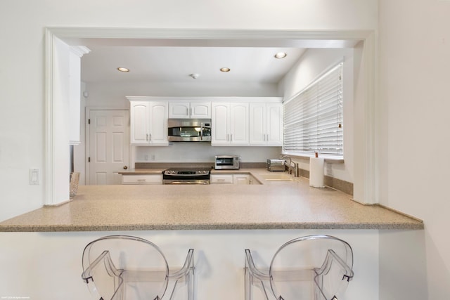 kitchen with light stone countertops, stainless steel appliances, white cabinetry, sink, and a breakfast bar