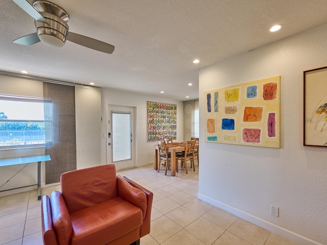 living area with a textured ceiling, ceiling fan, and light tile floors