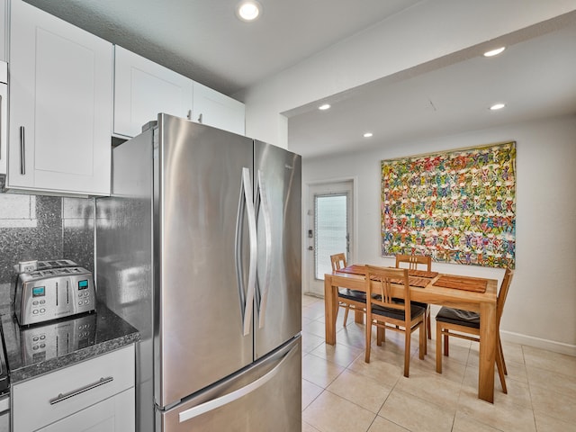 kitchen featuring tasteful backsplash, dark stone counters, stainless steel refrigerator, white cabinets, and light tile floors