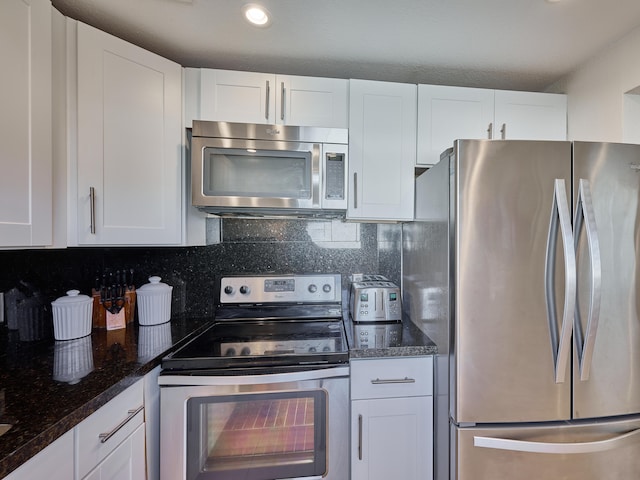 kitchen with appliances with stainless steel finishes, tasteful backsplash, dark stone counters, and white cabinetry