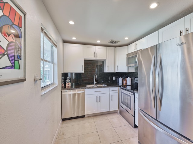 kitchen featuring white cabinets, light tile flooring, backsplash, appliances with stainless steel finishes, and sink