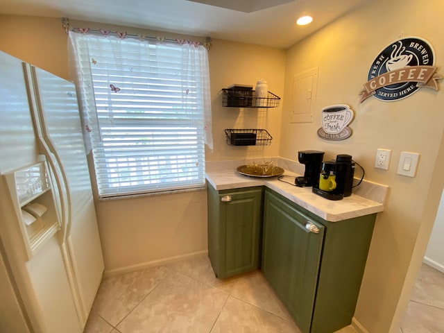 kitchen featuring white refrigerator with ice dispenser, light tile patterned floors, and green cabinets