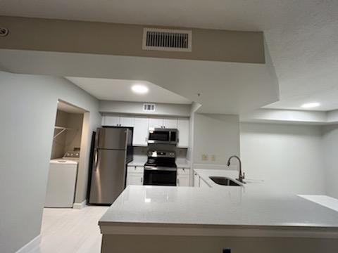 kitchen with kitchen peninsula, stainless steel appliances, washer / dryer, white cabinetry, and sink