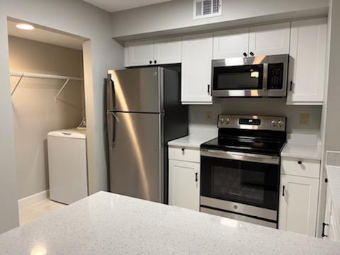 kitchen with light stone counters, appliances with stainless steel finishes, white cabinetry, and washer / dryer