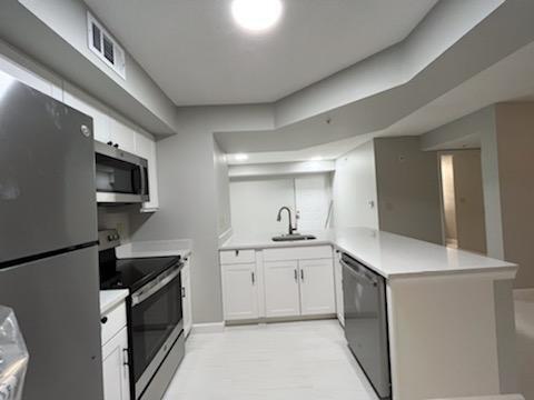 kitchen featuring kitchen peninsula, appliances with stainless steel finishes, white cabinetry, sink, and light tile floors