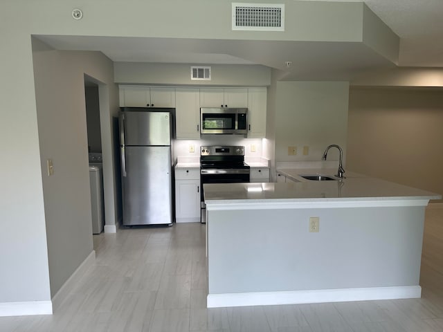 kitchen featuring kitchen peninsula, appliances with stainless steel finishes, washer / dryer, white cabinets, and sink