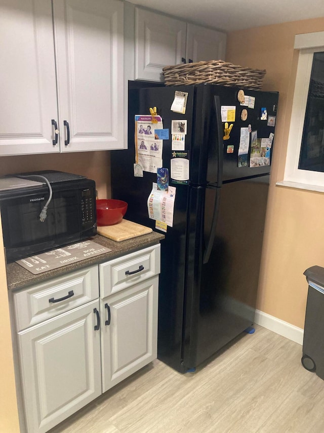 kitchen with light hardwood / wood-style flooring, white cabinetry, and black appliances