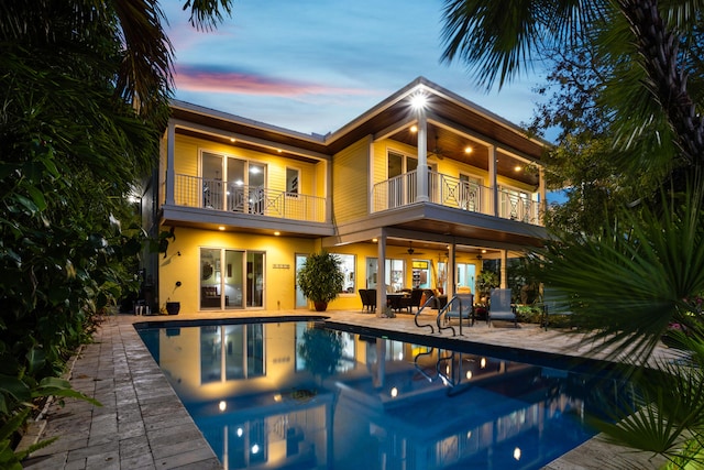 back house at dusk with ceiling fan, a balcony, and a patio