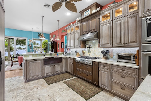 kitchen with light stone counters, dark brown cabinets, stainless steel appliances, sink, and hanging light fixtures