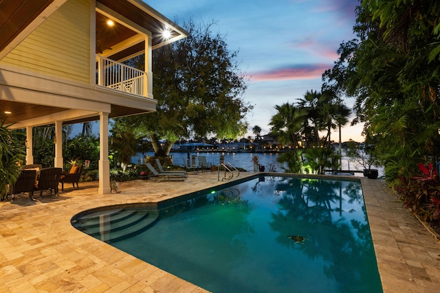 pool at dusk with a patio area and a water view