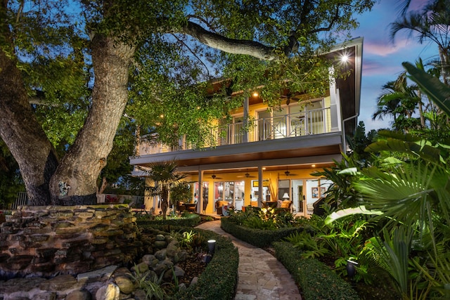 back house at dusk with ceiling fan and a balcony