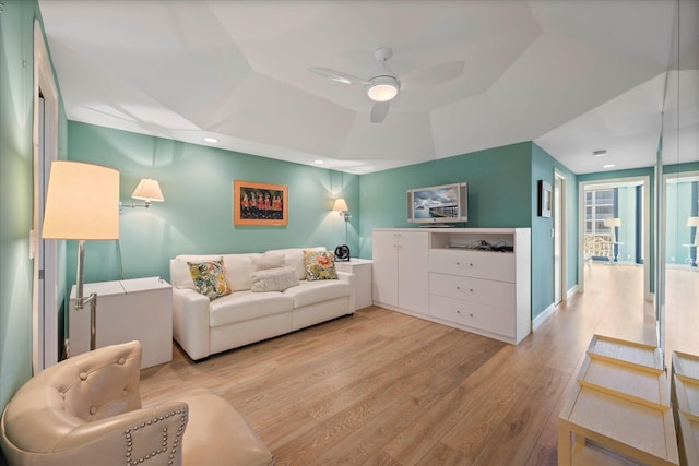 living room with light hardwood / wood-style flooring, ceiling fan, and a raised ceiling