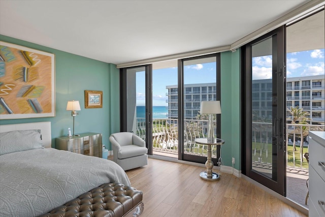 bedroom featuring multiple windows, wood-type flooring, access to outside, and a water view