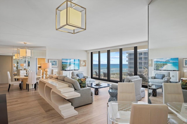 living room with a water view, hardwood / wood-style floors, a wall of windows, and a chandelier