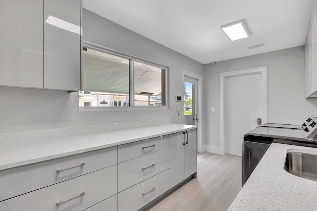 kitchen featuring light wood-type flooring, light stone counters, sink, washer / clothes dryer, and white cabinetry