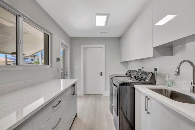 laundry area featuring washer and dryer, light hardwood / wood-style floors, cabinets, and sink