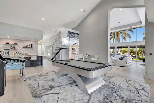 recreation room with bar, a towering ceiling, billiards, and light hardwood / wood-style flooring