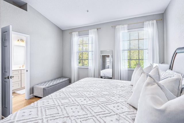 bedroom featuring ensuite bath, lofted ceiling, and light wood-type flooring