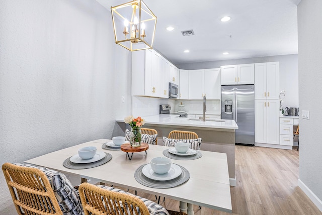 kitchen with appliances with stainless steel finishes, white cabinets, sink, light wood-type flooring, and kitchen peninsula