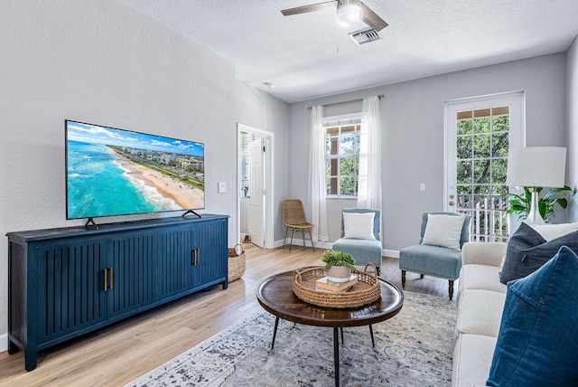 living room featuring light hardwood / wood-style flooring, ceiling fan, and a textured ceiling