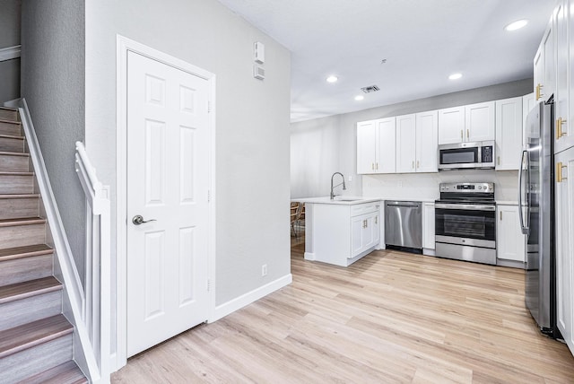 kitchen with kitchen peninsula, appliances with stainless steel finishes, light hardwood / wood-style floors, white cabinetry, and sink