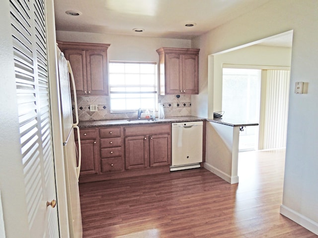 kitchen with white appliances, dark wood-type flooring, backsplash, kitchen peninsula, and sink