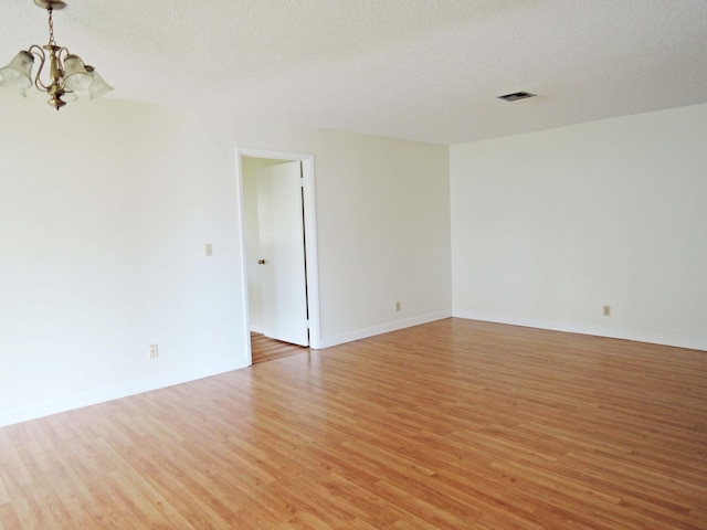 spare room with a textured ceiling, a notable chandelier, and light wood-type flooring