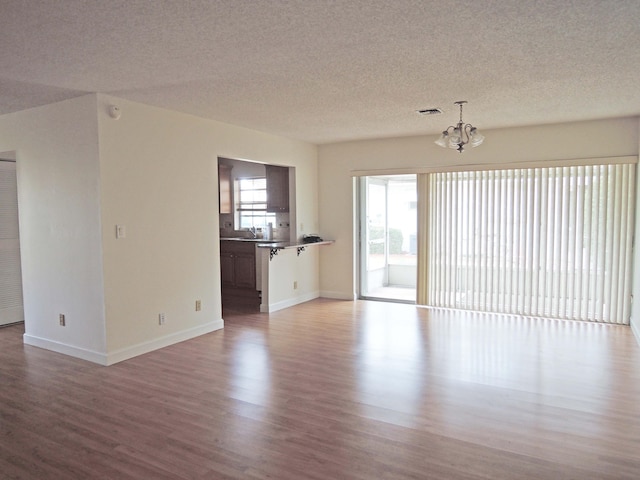 unfurnished living room featuring wood-type flooring, a textured ceiling, and an inviting chandelier