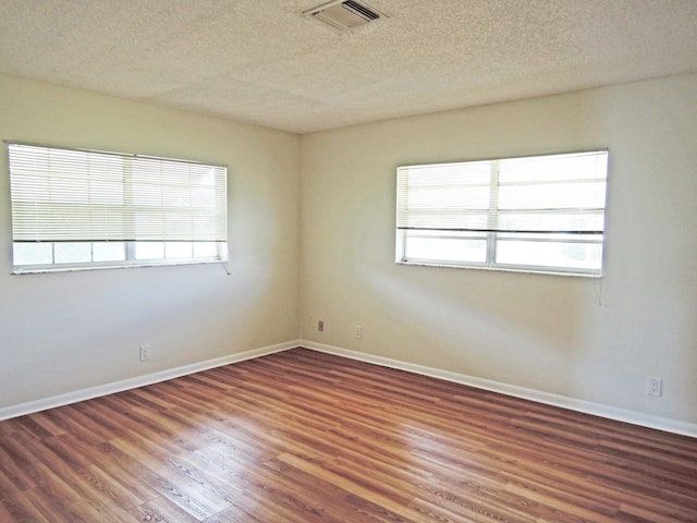 empty room with dark hardwood / wood-style floors, plenty of natural light, and a textured ceiling