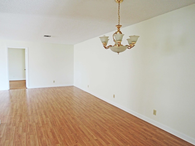 unfurnished room with a textured ceiling, a notable chandelier, and hardwood / wood-style floors