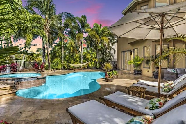 pool at dusk with a patio area and an in ground hot tub