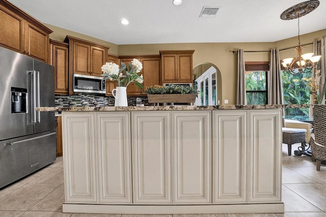 kitchen with light tile patterned flooring, a notable chandelier, decorative backsplash, a kitchen island, and appliances with stainless steel finishes