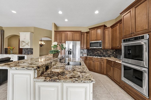 kitchen with sink, stainless steel appliances, an inviting chandelier, backsplash, and a spacious island