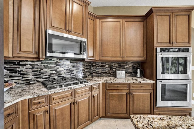 kitchen with decorative backsplash, light stone counters, light tile patterned floors, and stainless steel appliances