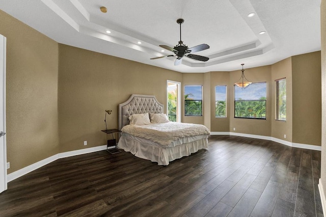 unfurnished bedroom with a tray ceiling, ceiling fan, and dark wood-type flooring