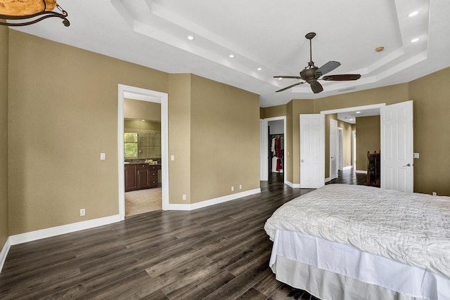 bedroom featuring dark wood-type flooring, a walk in closet, ceiling fan, connected bathroom, and a tray ceiling