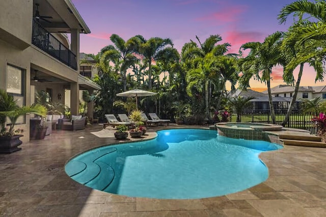 pool at dusk with ceiling fan, a patio area, and an in ground hot tub