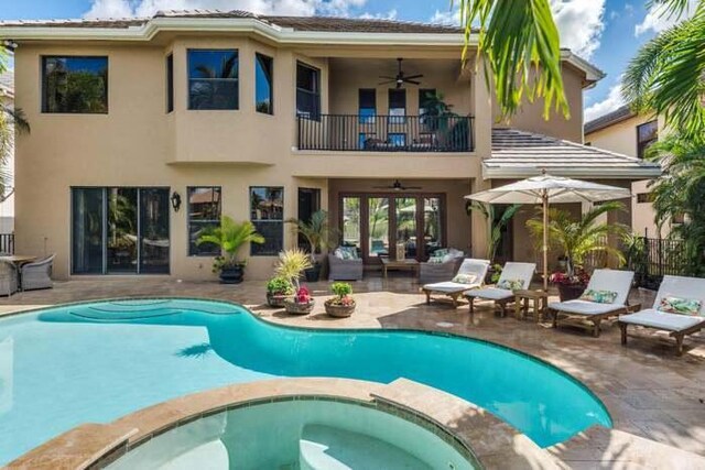 back of house featuring french doors, a balcony, a pool with hot tub, ceiling fan, and a patio area