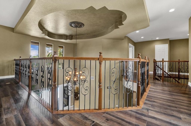 corridor with a tray ceiling, dark hardwood / wood-style flooring, and a notable chandelier