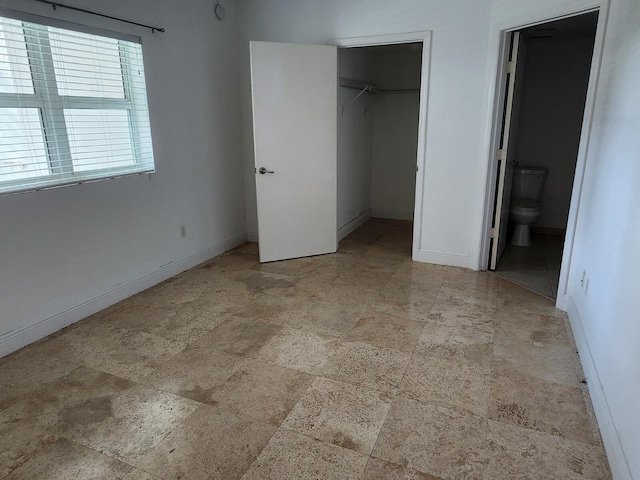 unfurnished bedroom with connected bathroom, a closet, light tile flooring, and a spacious closet