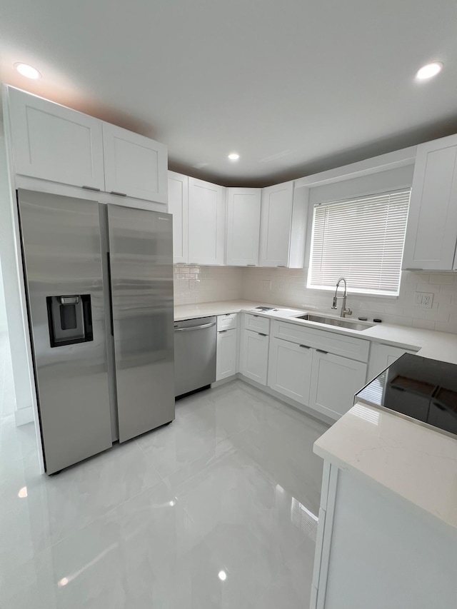 kitchen featuring light stone counters, sink, white cabinetry, stainless steel appliances, and decorative backsplash